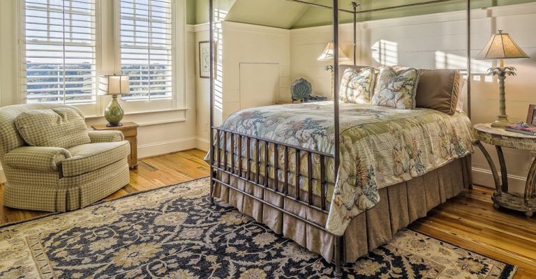 Elegant bedroom featuring a traditional floral Oriental area rug, wooden flooring, a four-poster bed, and a comfortable armchair